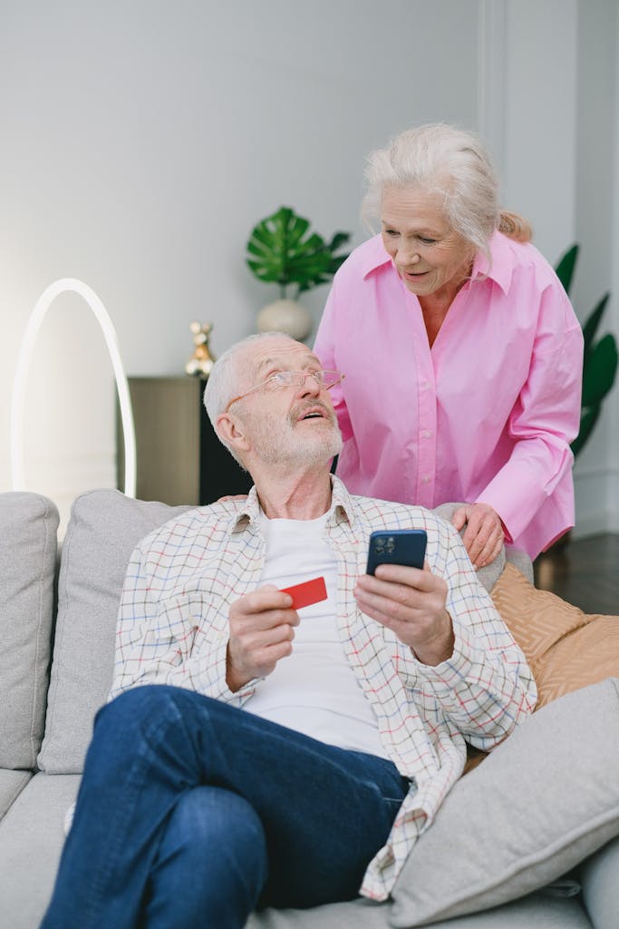 Elderly couple using a mobile phone and credit card for online shopping at home.